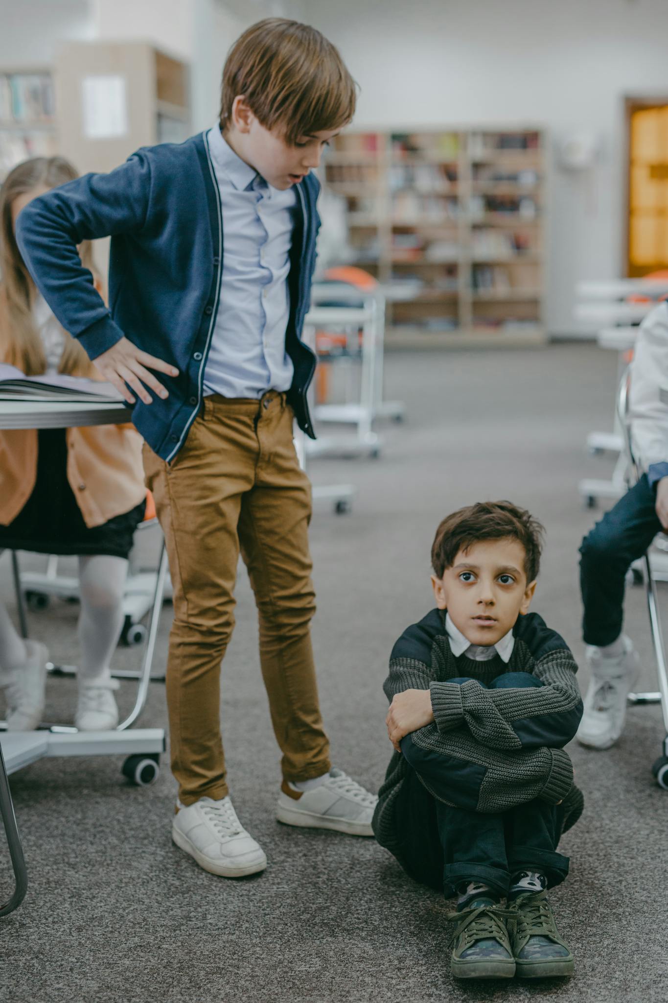 Two boys in a school library scene depicting a bullying incident, highlighting peer conflicts.